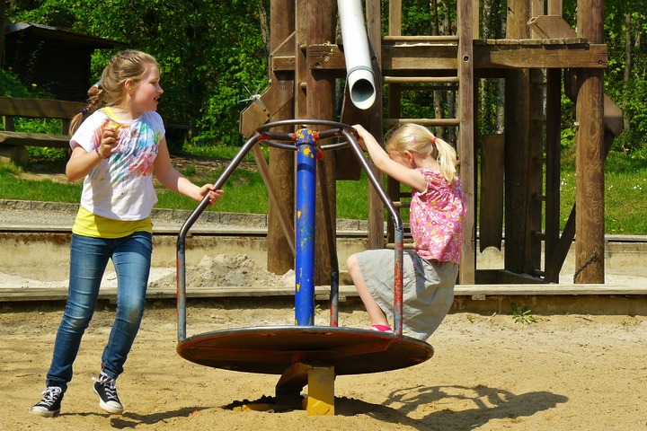 RSI-klachten kinderen: verslaafd aan de smartphone, twee meisjes op een draaimolen in een speeltuin